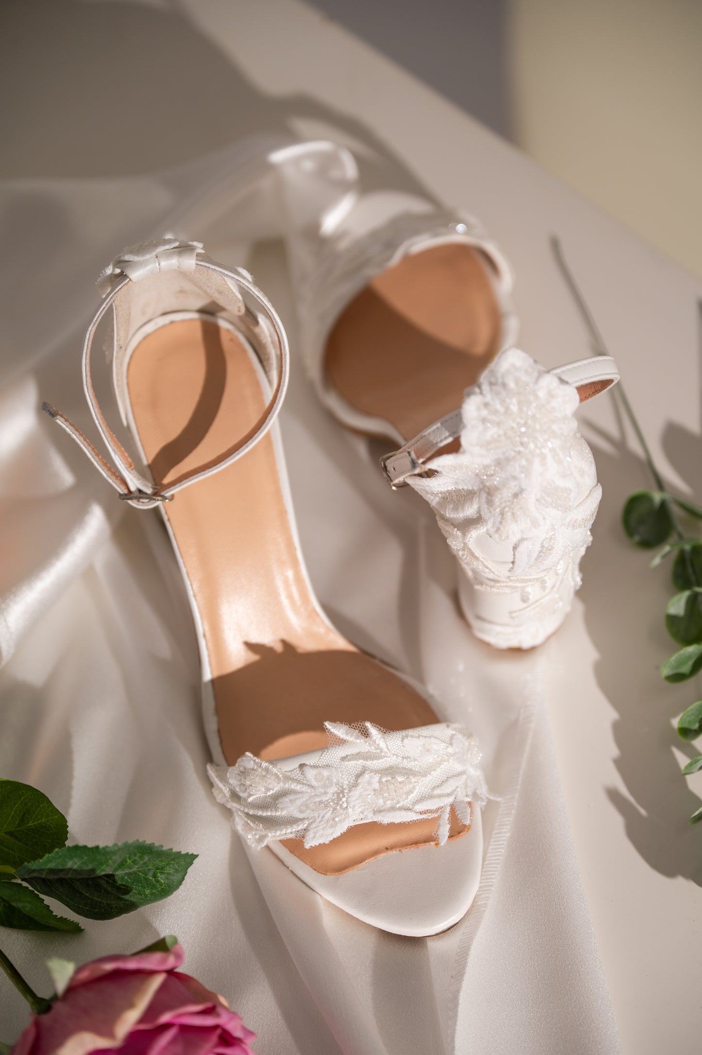 A pair of white block heel wedding shoes with floral lace detailing and ankle straps