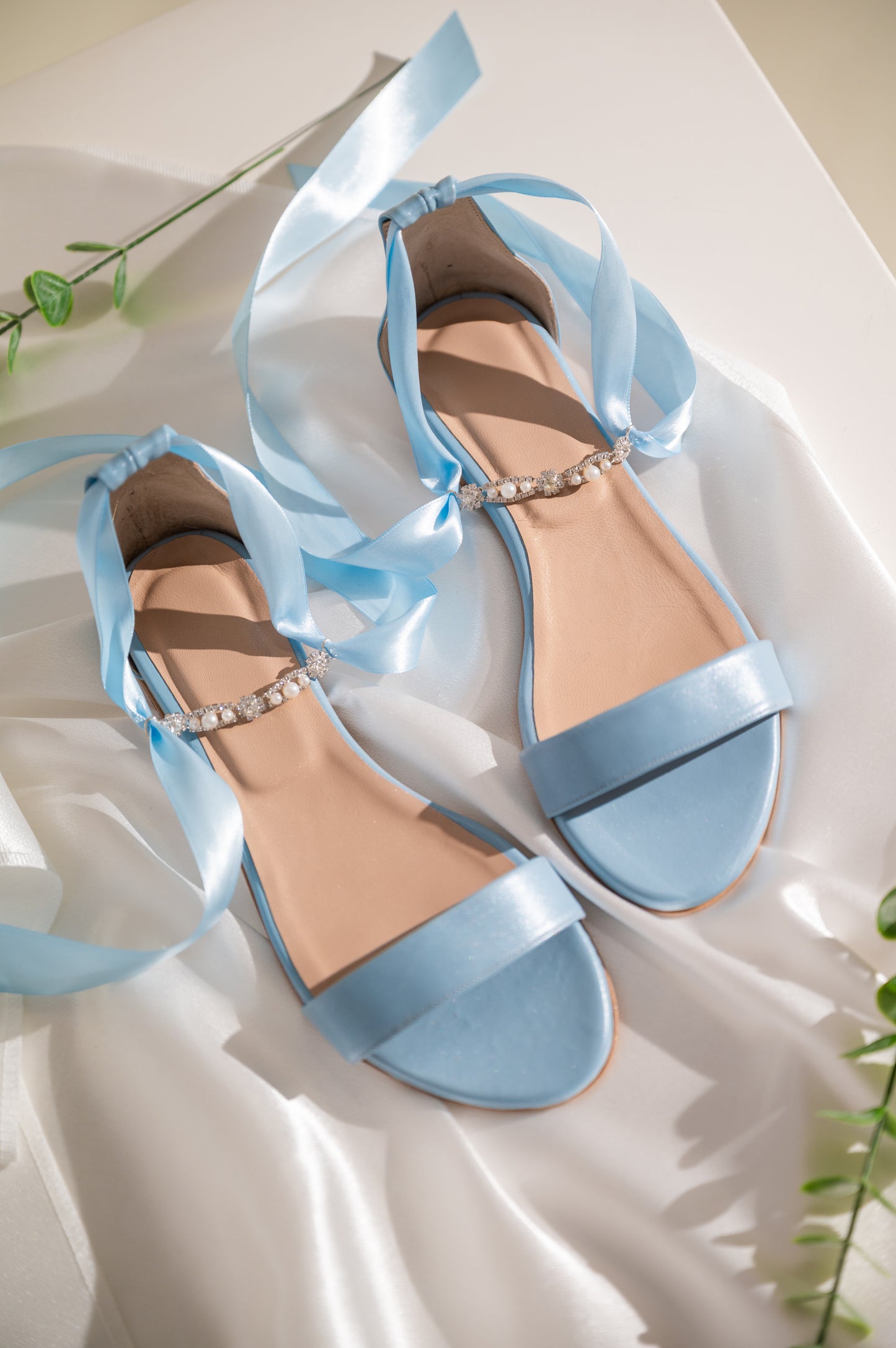 A pair of blue flat wedding sandals with wide straps and a buckle closure, displayed on a white fabric surface.