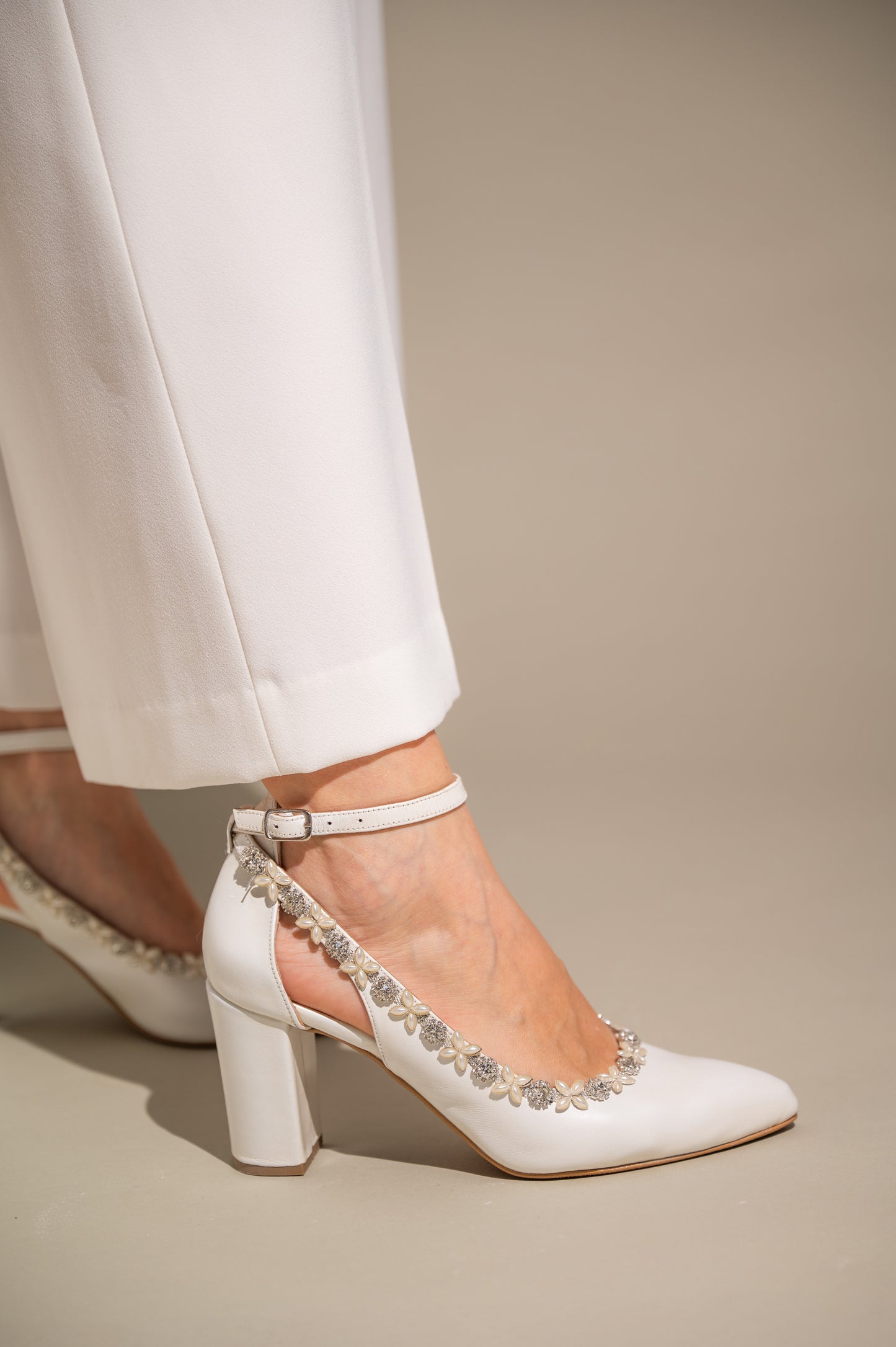 A close-up of white leather high-heeled wedding shoes with ankle straps and rhinestone embellishments.