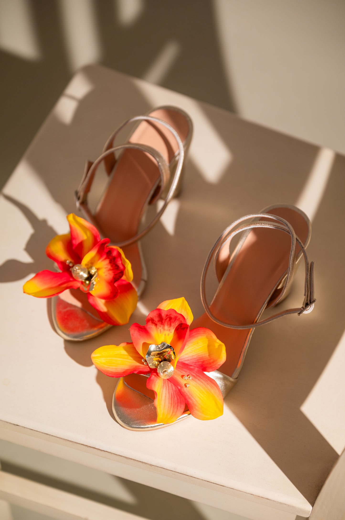 A pair of gold block heel sandals with a floral design on the straps.