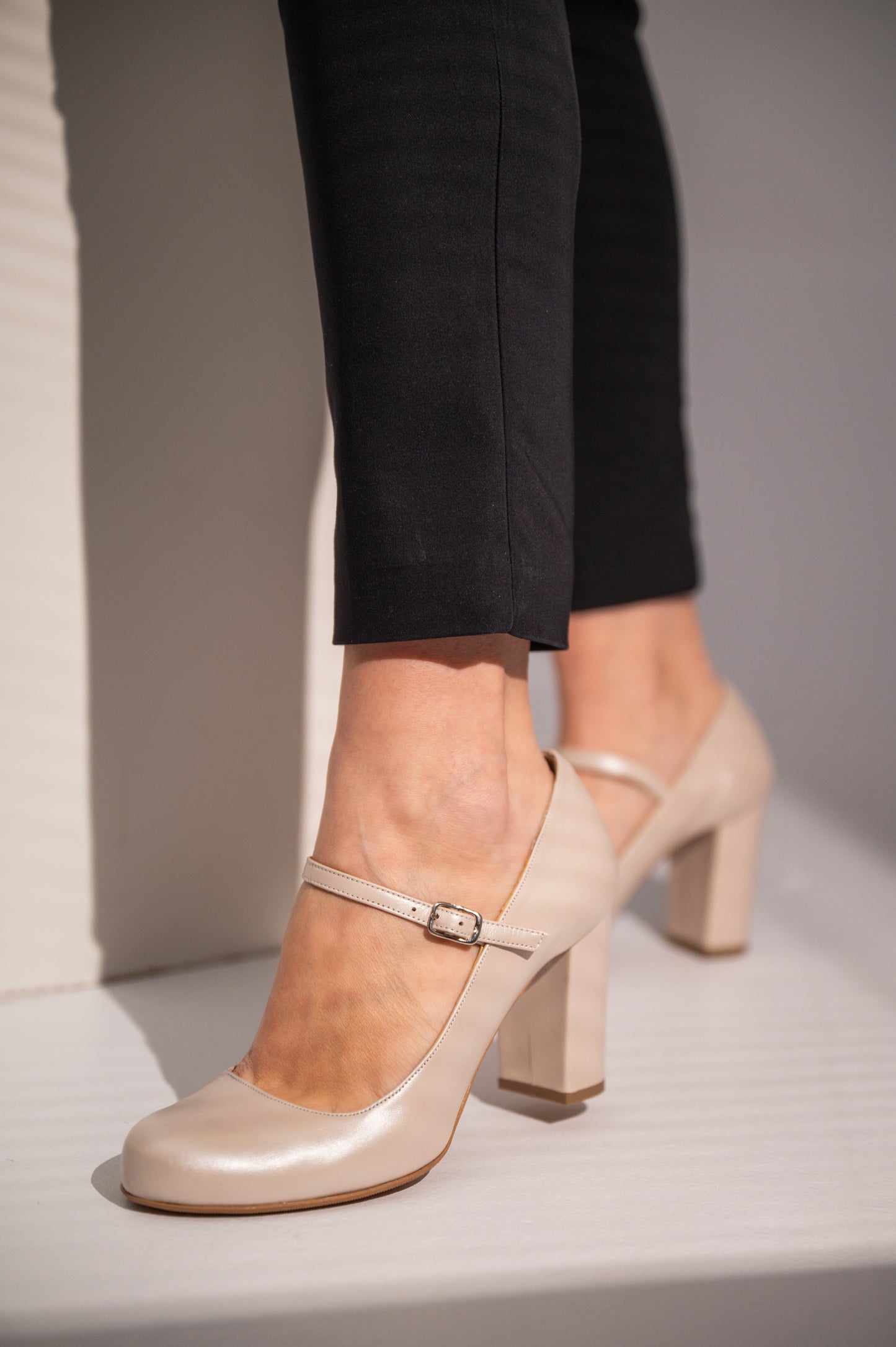 A close-up of a woman's foot wearing an ivory-colored heel with a buckle strap and block heel.