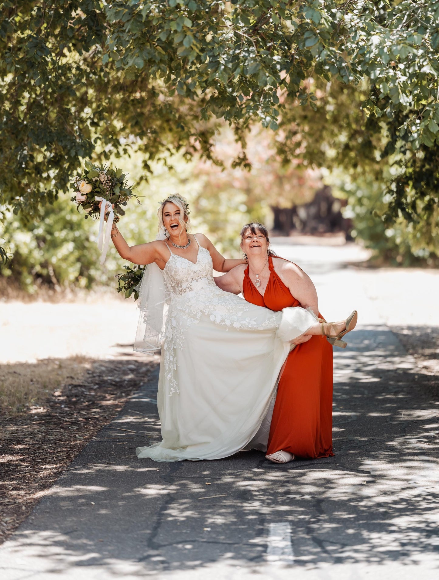 Two women in wedding dresses standing under a tree