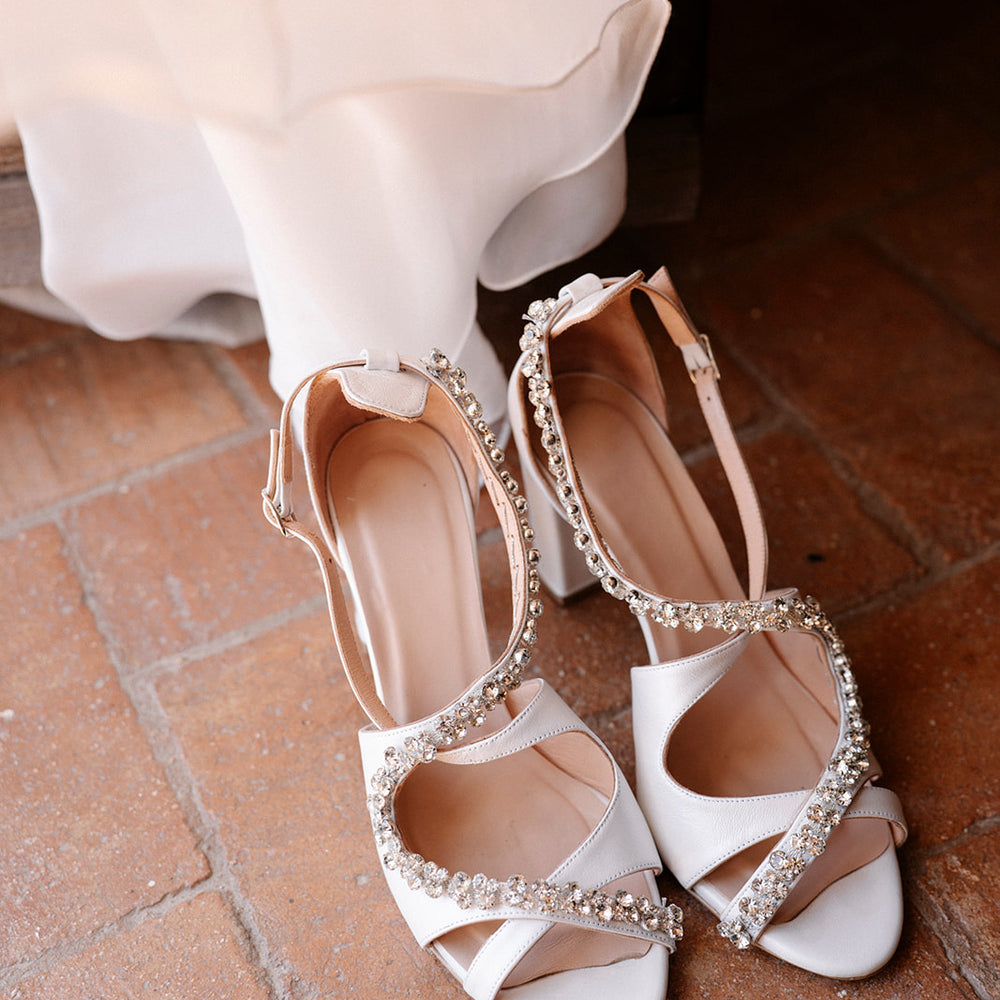 White wedding shoes with embellishments on a brick floor