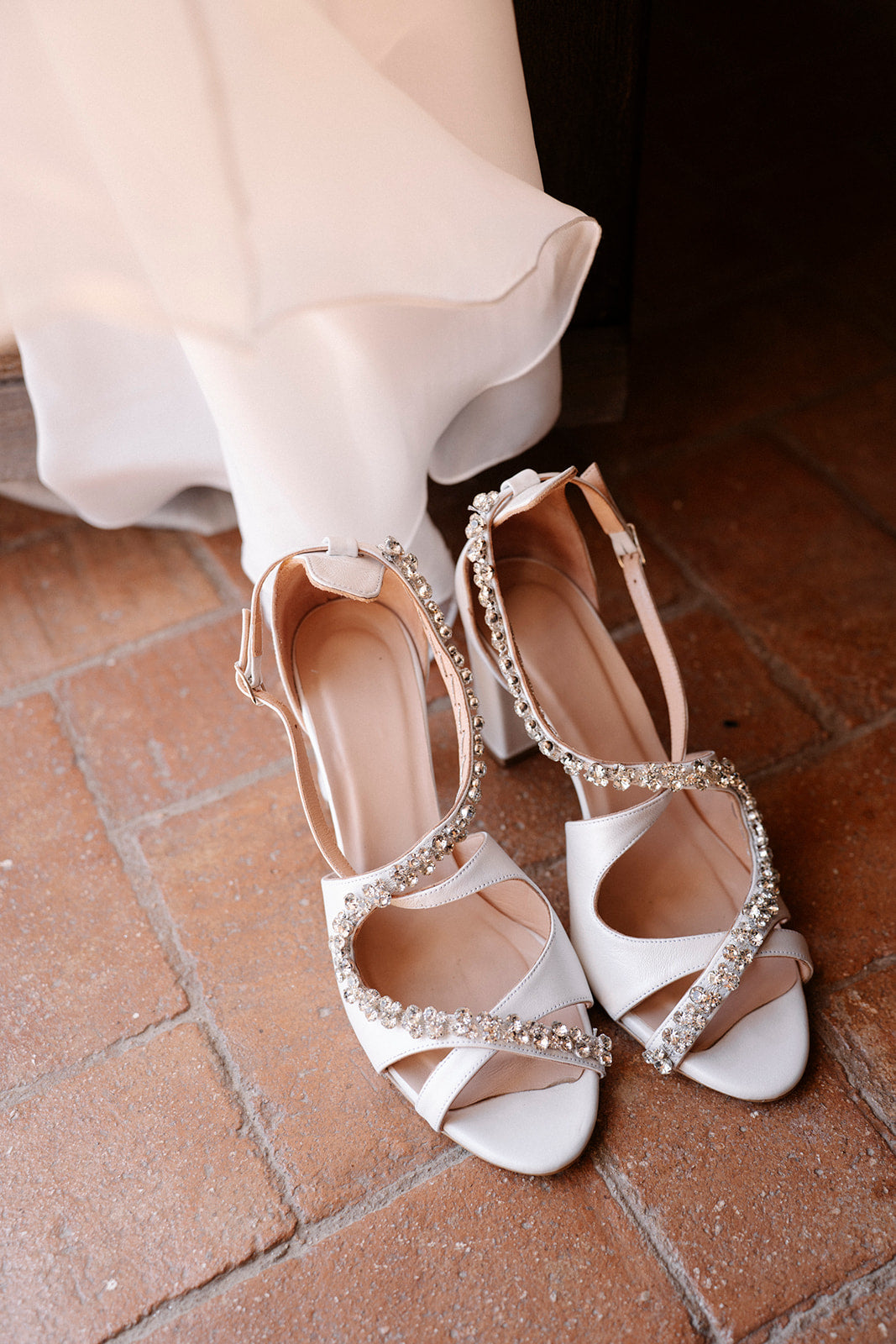 White wedding shoes with embellishments on a brick floor