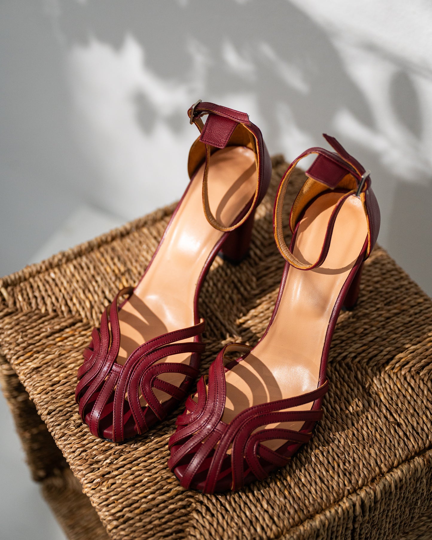 Pair of burgundy mary janes high-heeled sandals on a woven surface with a neutral background