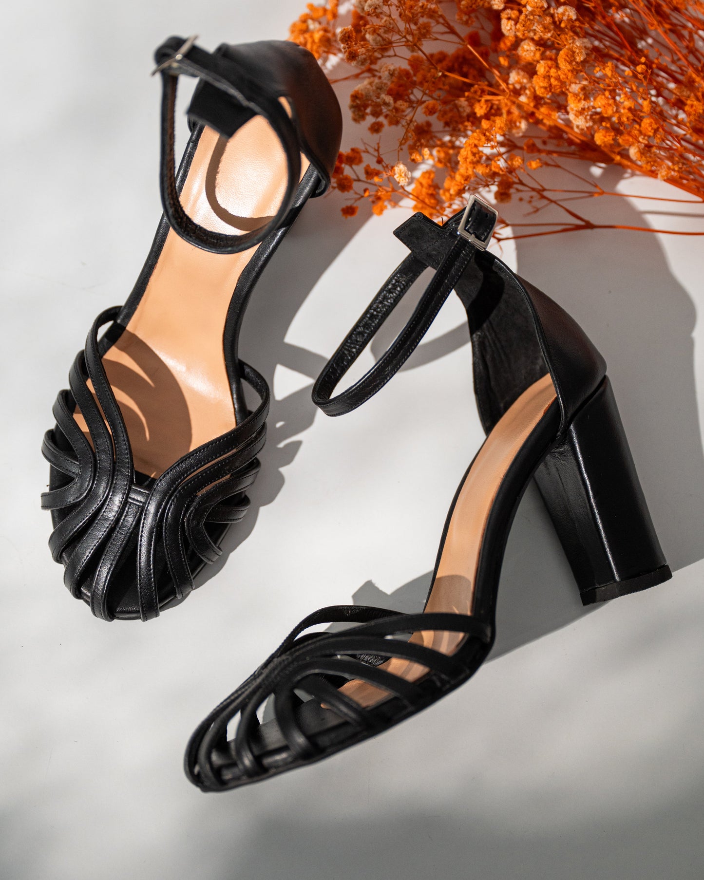 Black high-heeled sandals on a light background with orange decorative elements.