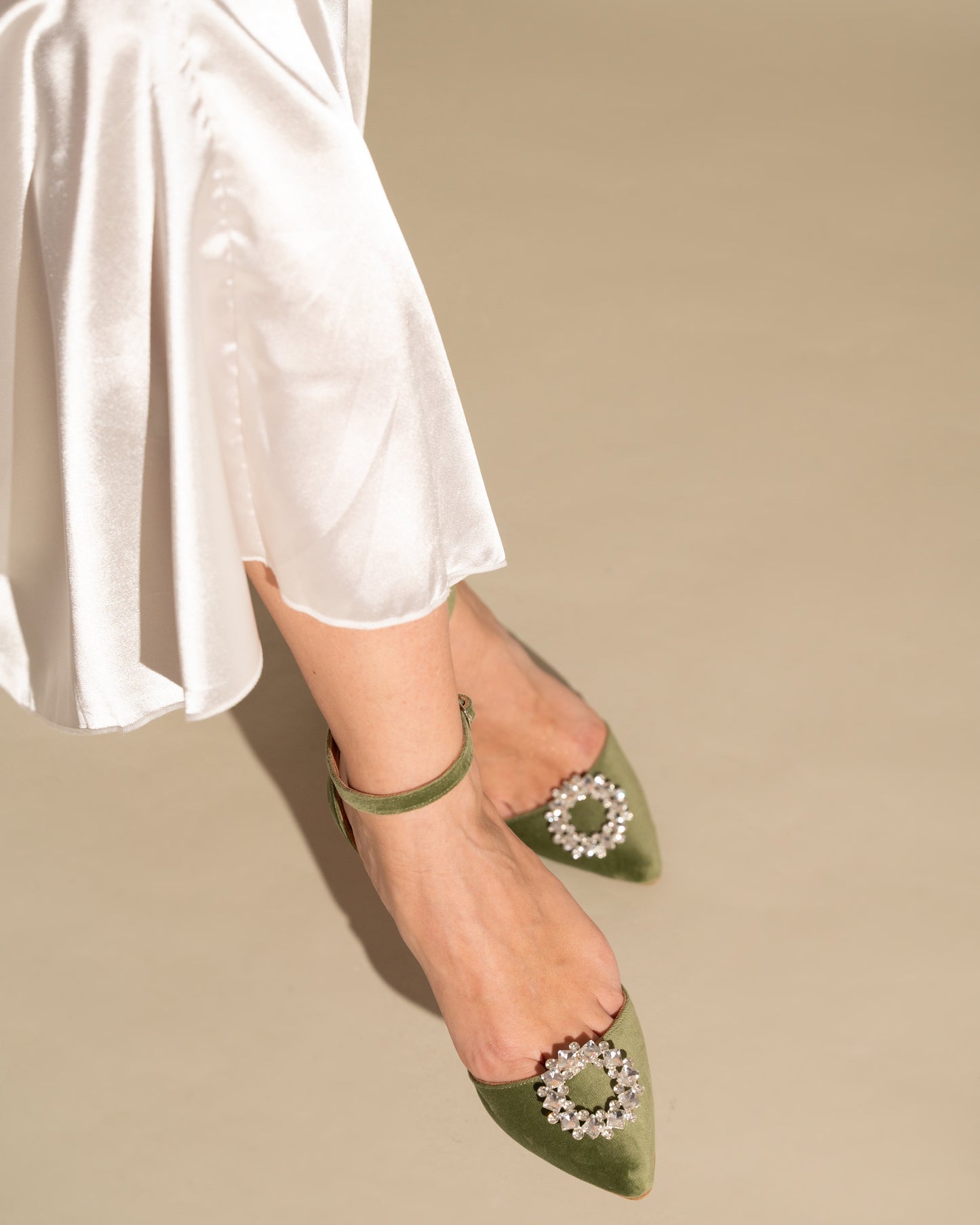 Green pointed-toe shoes with embellishments worn with white pants on a beige background