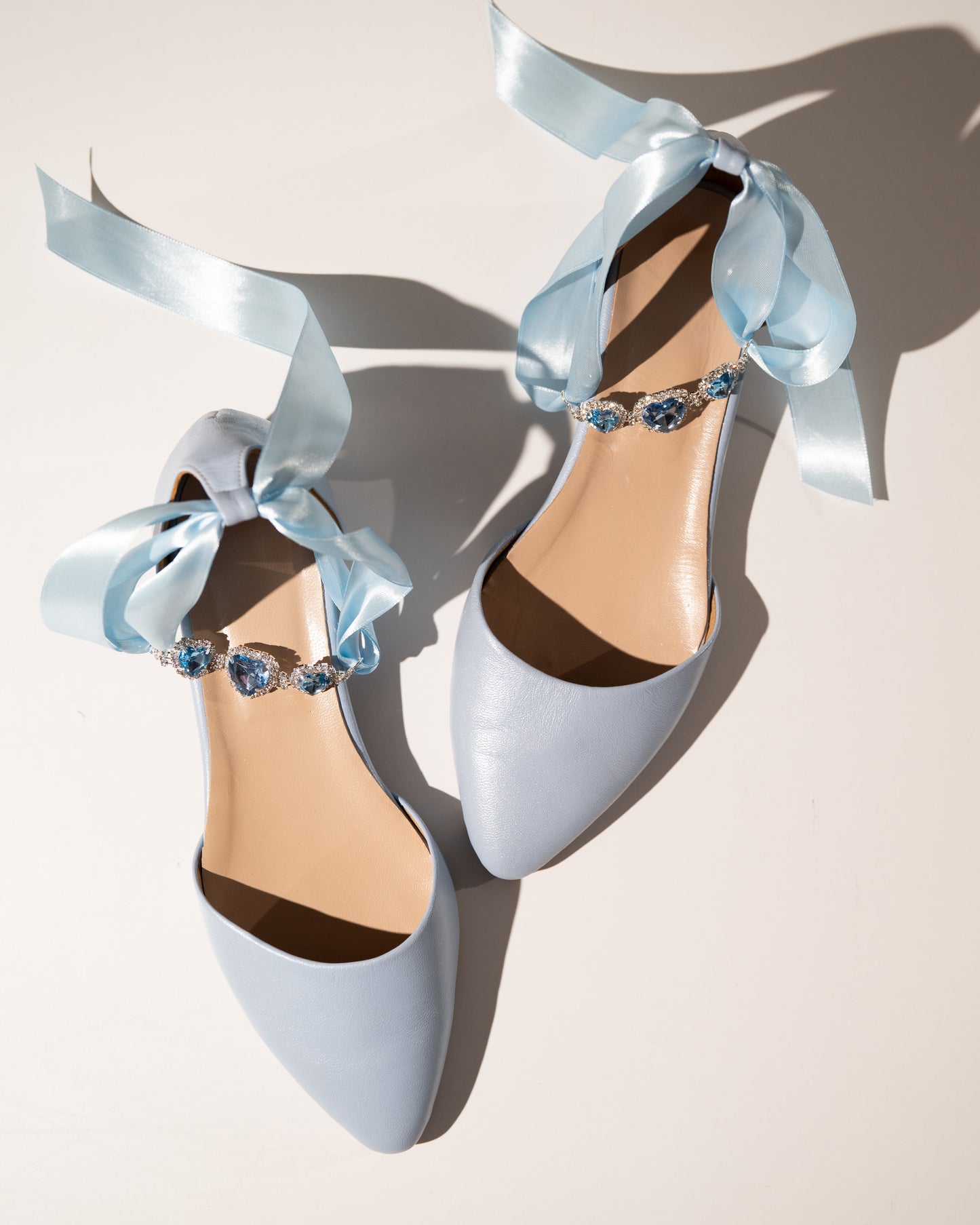 Pair of light blue high-heeled shoes with decorative ribbons and beads on a neutral background