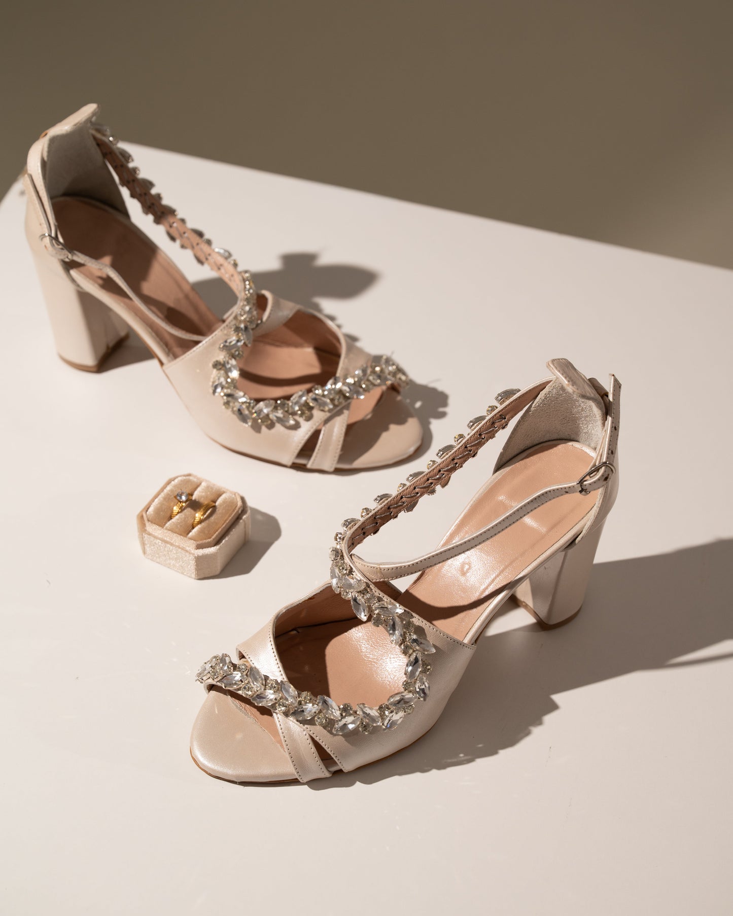 Pair of ivory high-heeled sandals with crystal embellishments on a light surface.