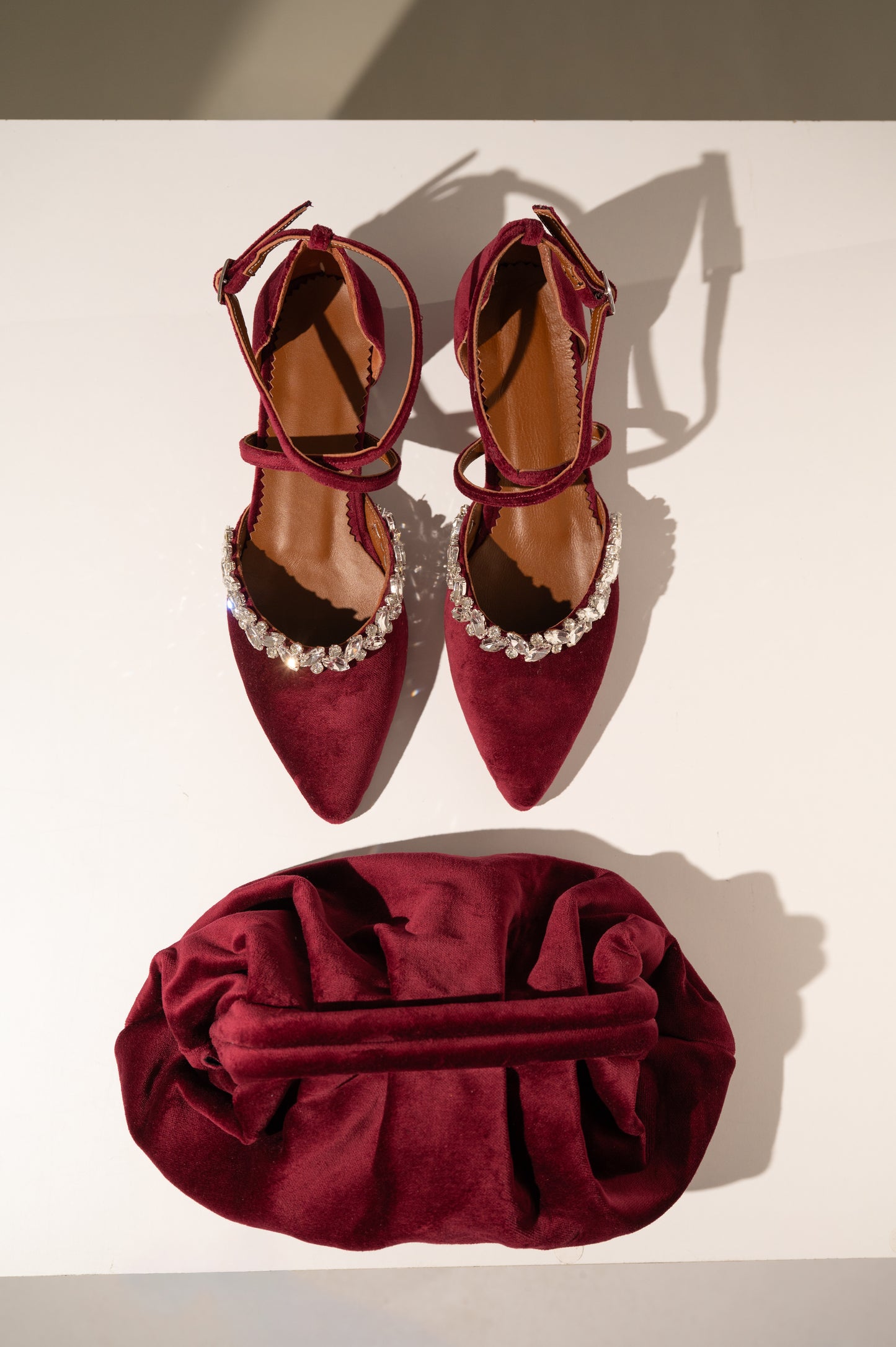 Pair of maroon high-heeled shoes with pearl straps and a matching red clutch bag on a white background.