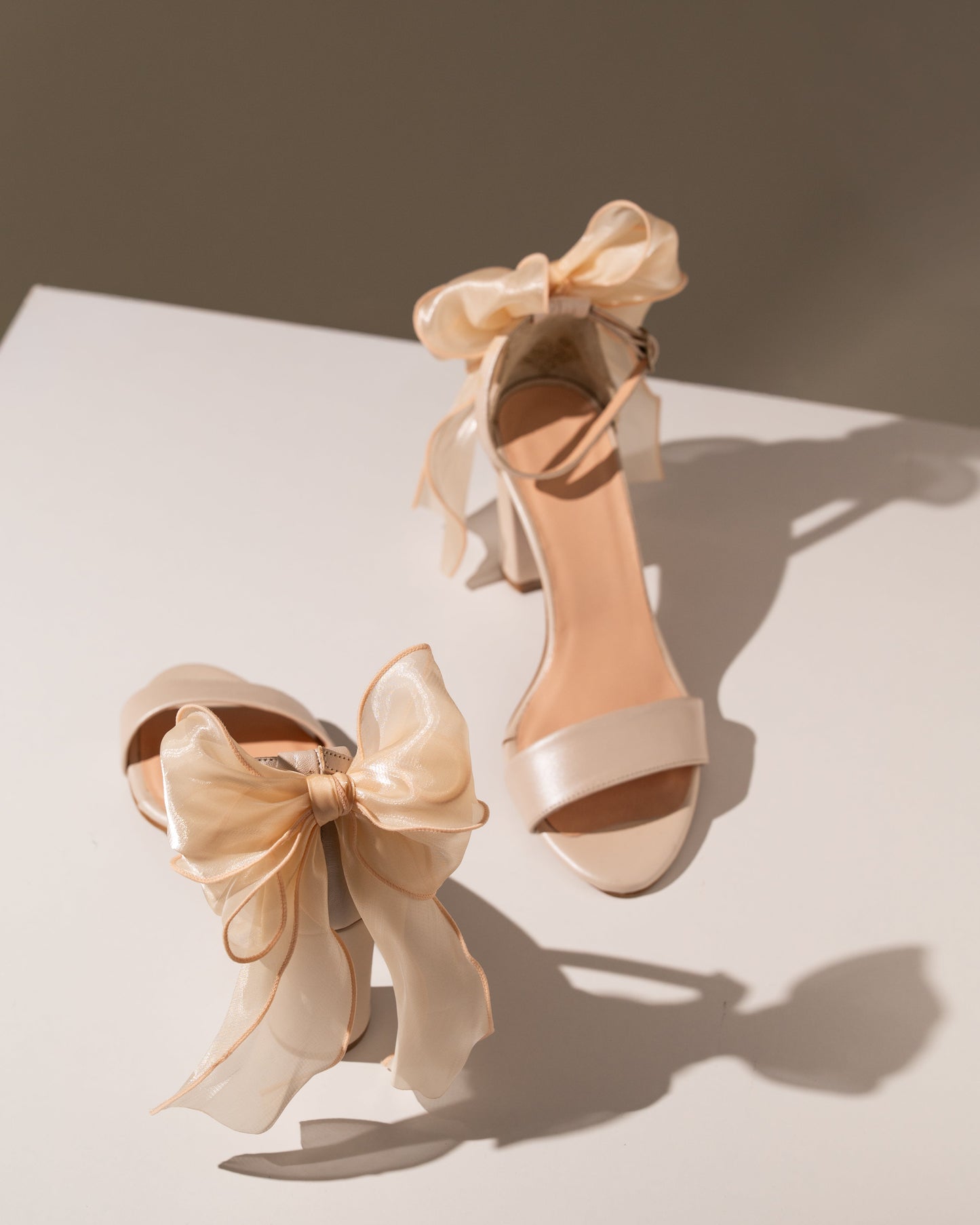 Pair of cream high-heeled shoes with large ribbons on a light background