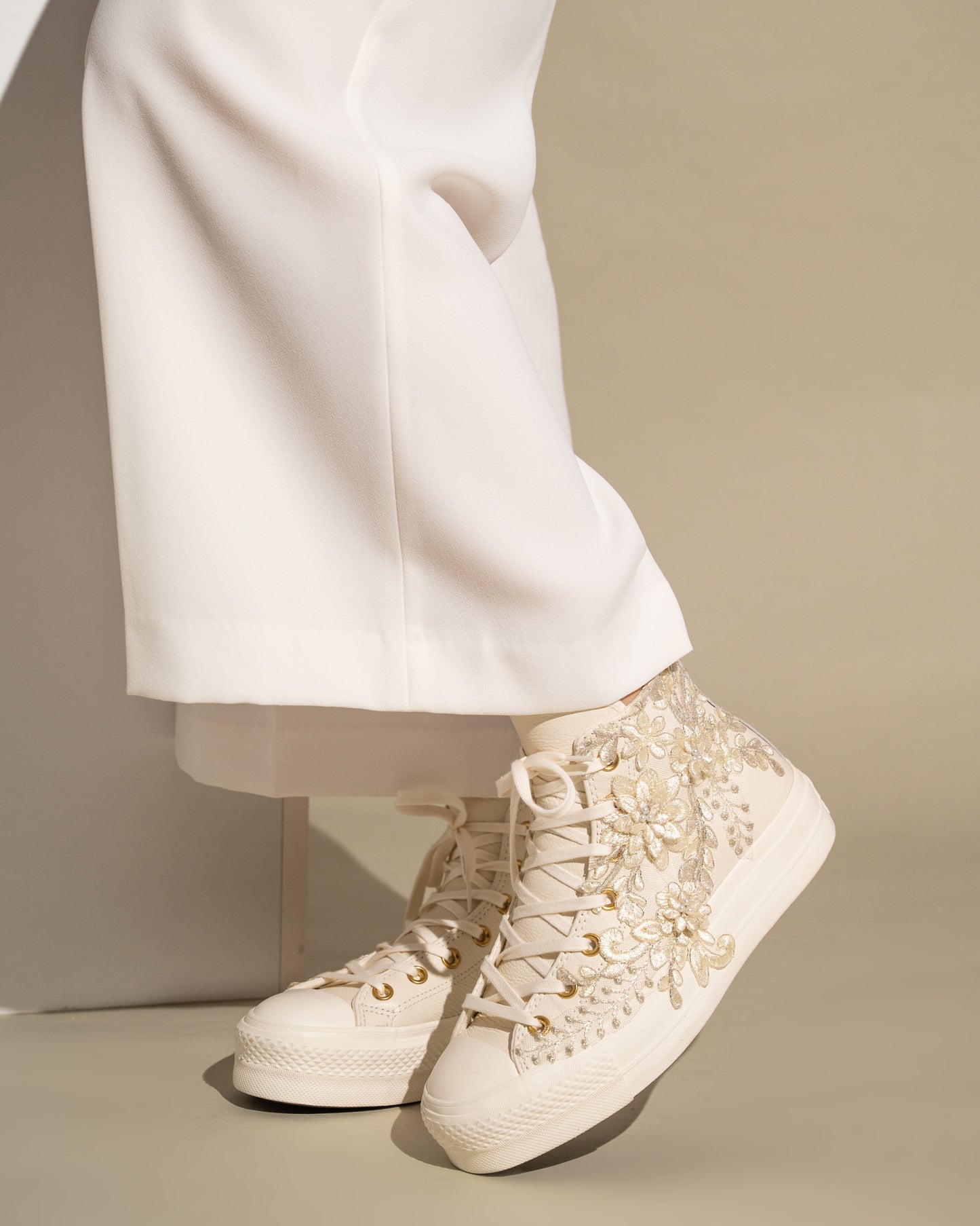Ivory lace-up high-top sneakers worn with white pants on a neutral background
