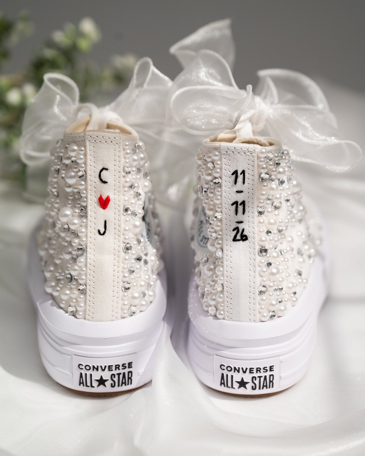 White Converse All Star high-top sneakers with rhinestone embellishments and personalized details on a white surface.