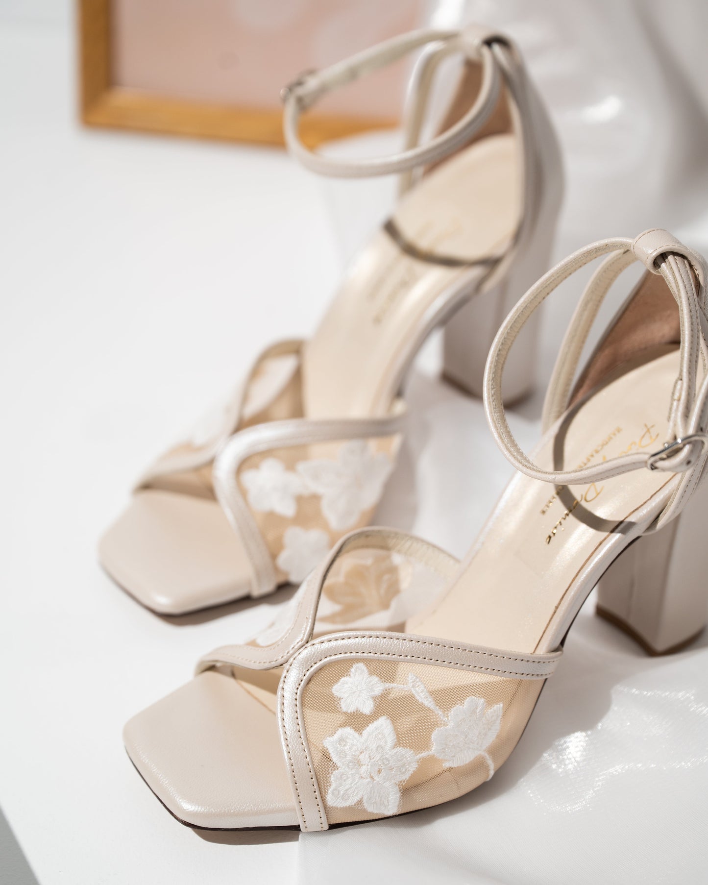 Beige high-heeled shoes with floral lace details on a white surface.