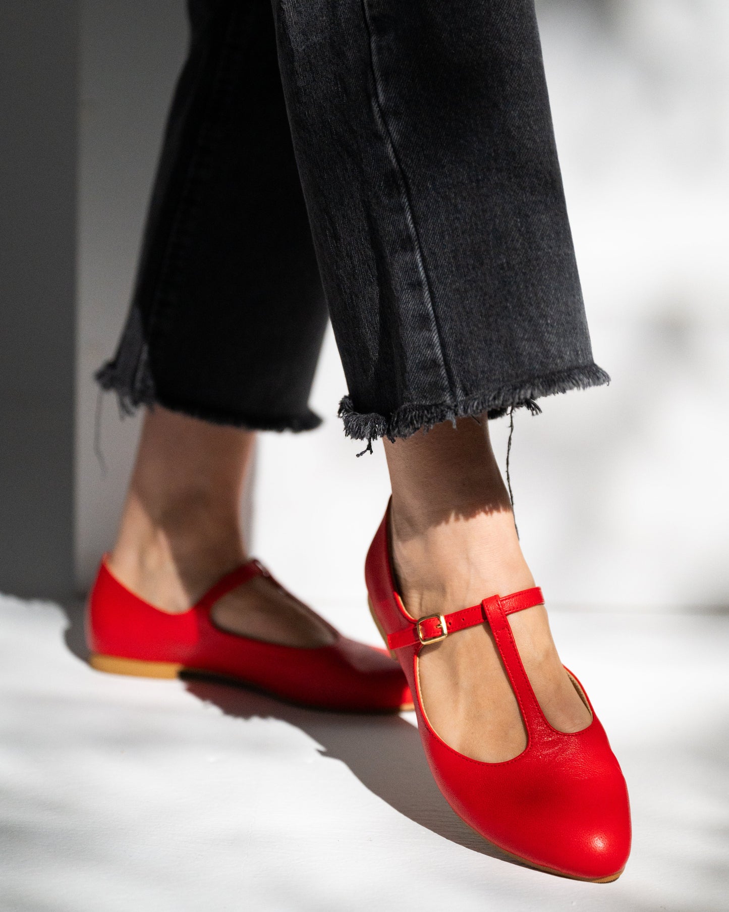 Red shoes worn with black jeans on a neutral background