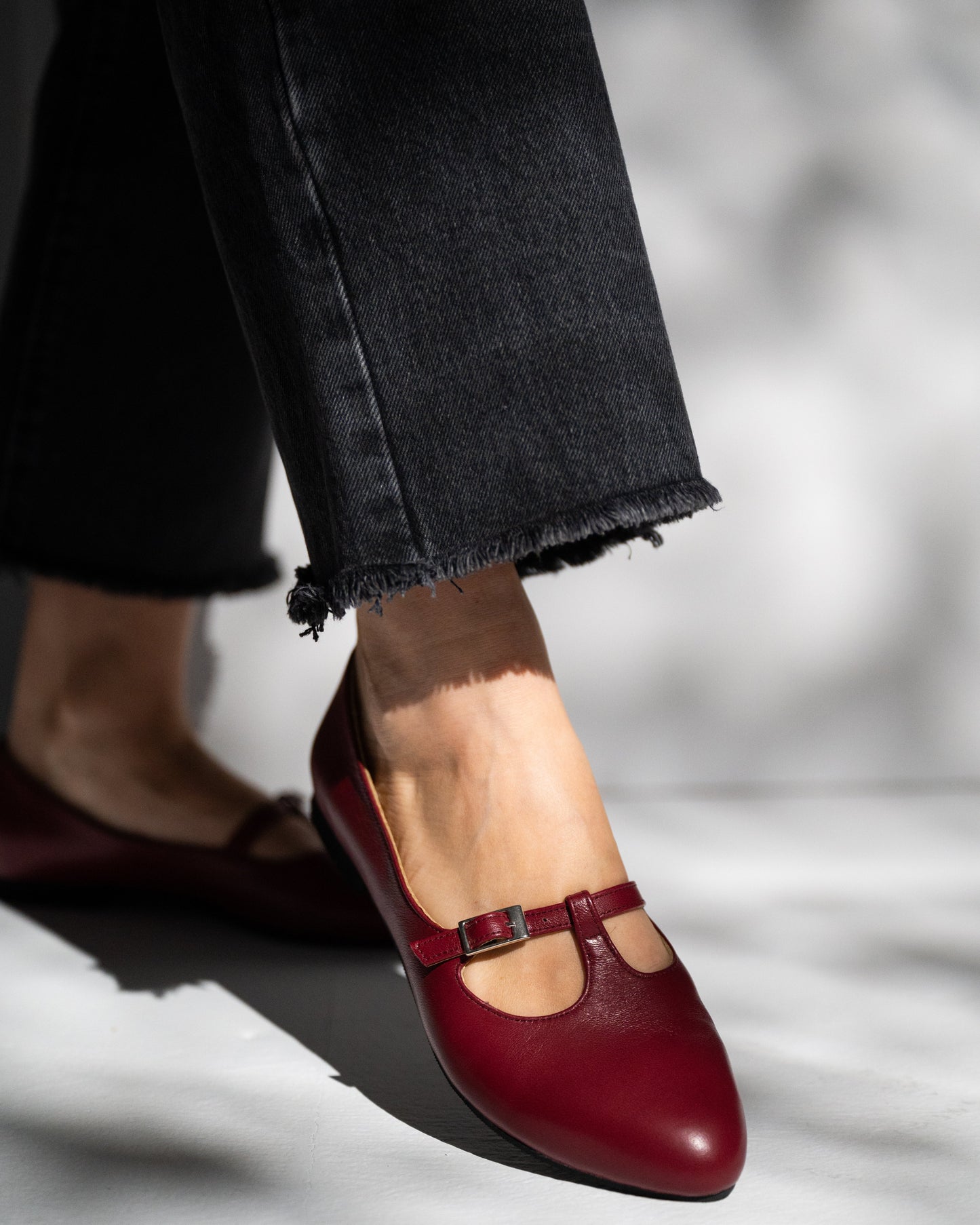 burgundy mary jane shoes worn with black jeans on a blurred background