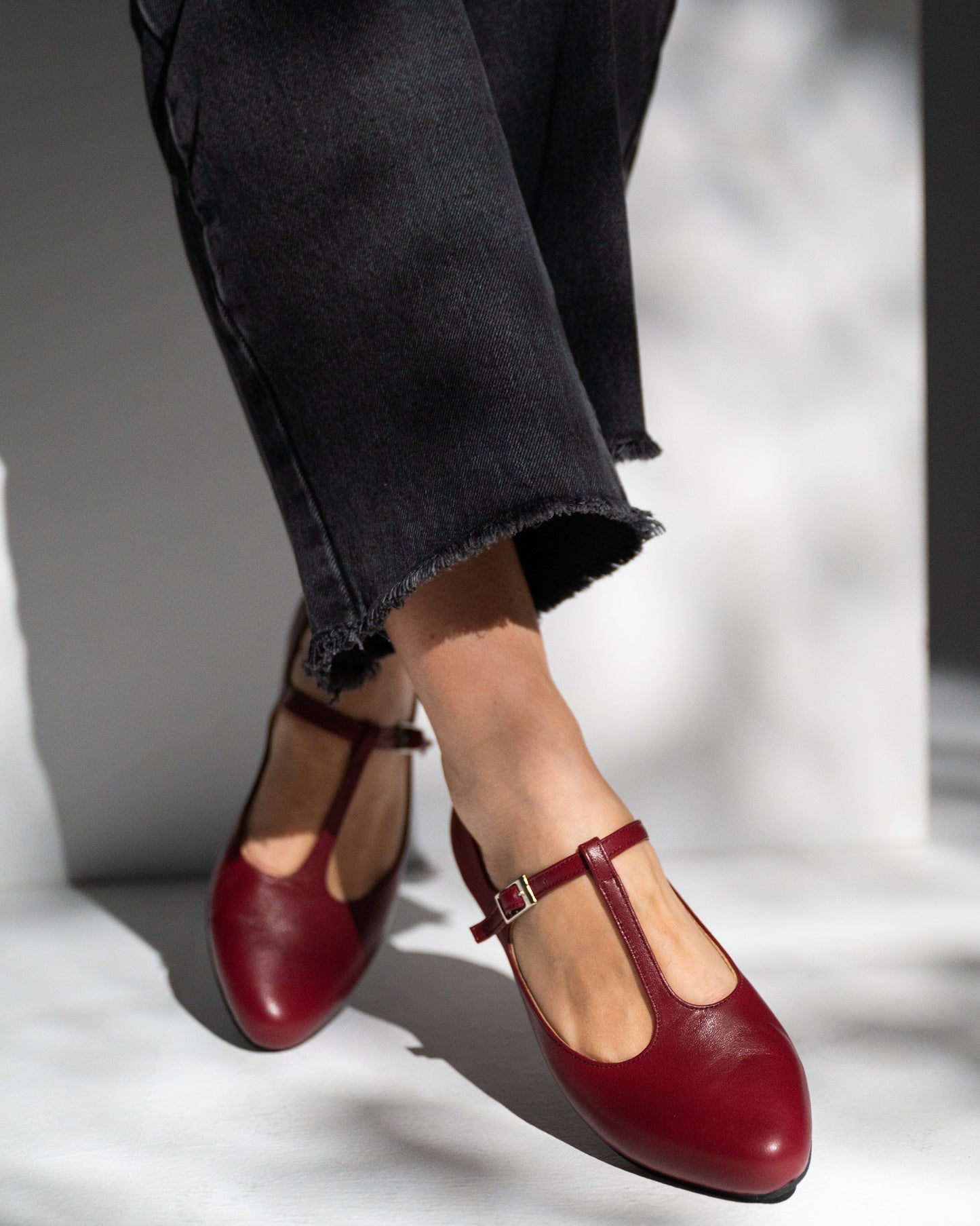 burgundy mary jane shoes worn with black pants on a light background