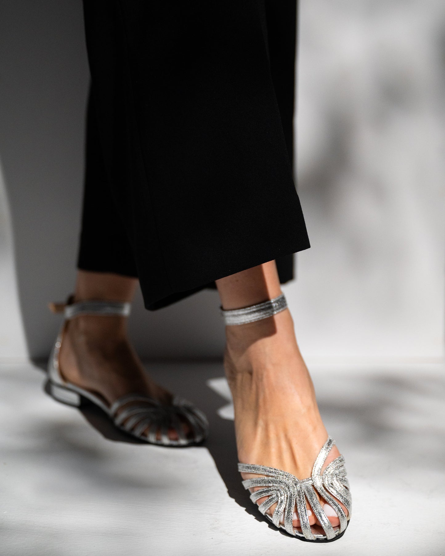 Silver sandals worn with black pants on a neutral background