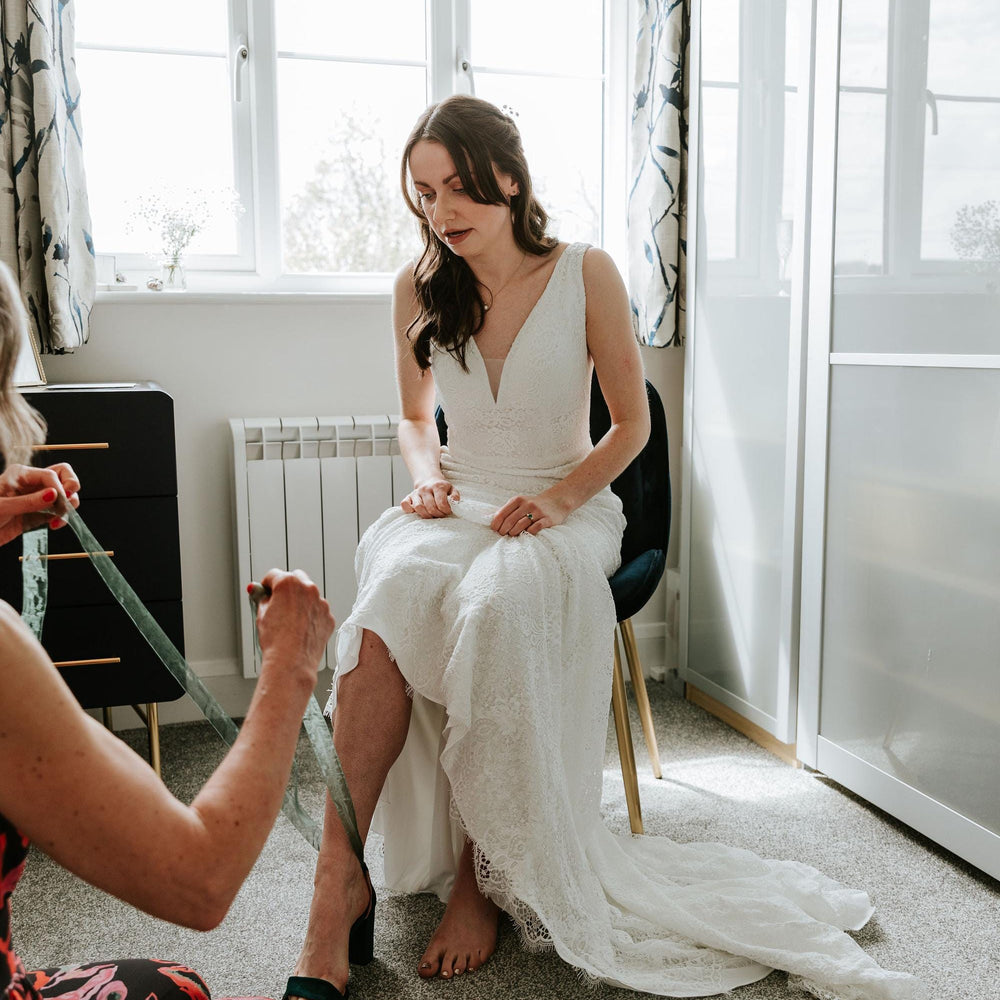 Woman in a white dress sitting on a chair with another person taking a photo.
