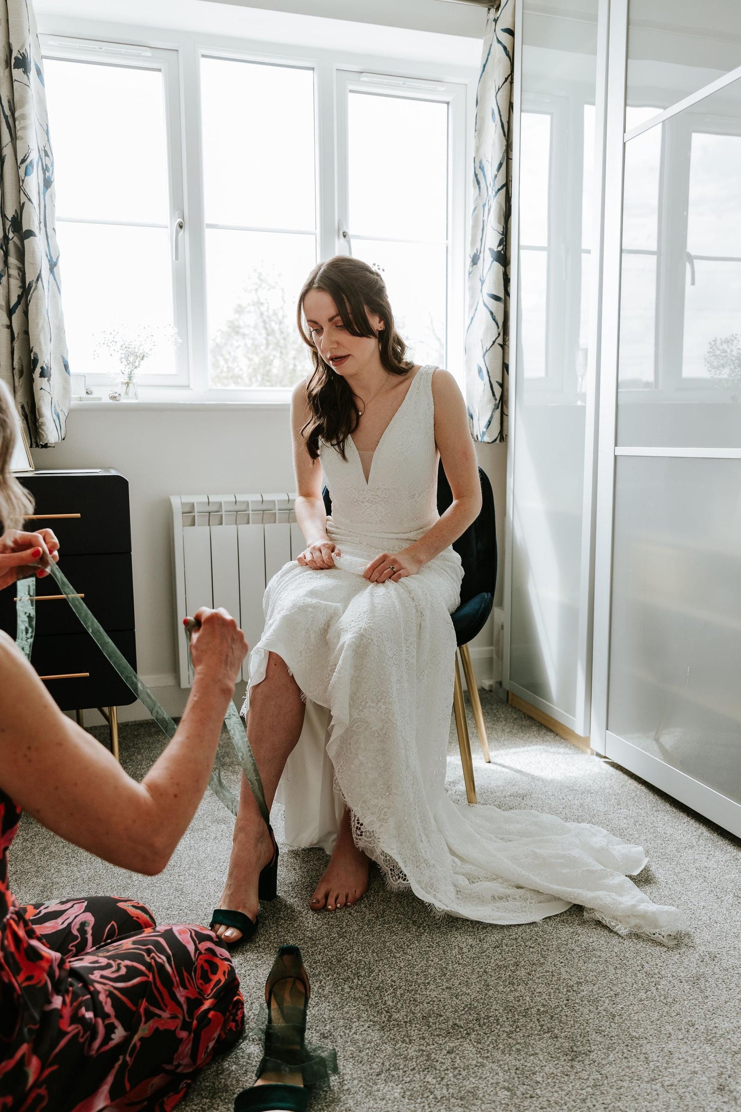 Woman in a white dress sitting on a chair with another person taking a photo.