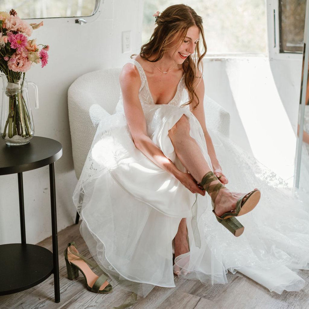 Woman in a white dress sitting inside a vehicle, adjusting her green sandals.