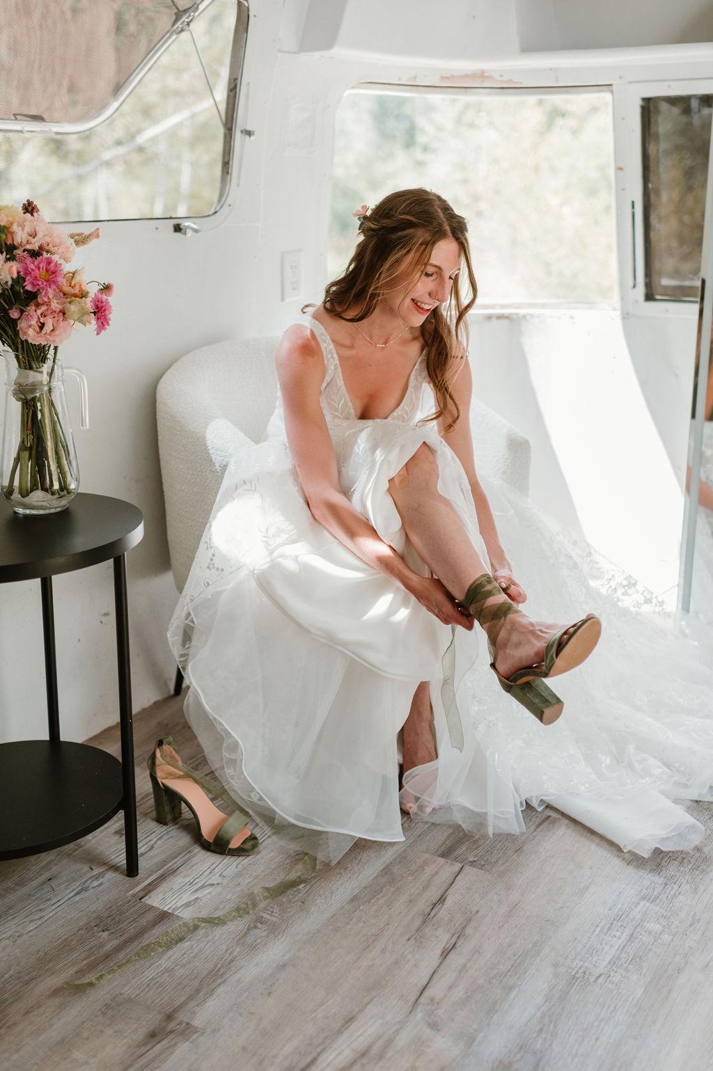 Woman in a white dress sitting inside a vehicle, adjusting her green sandals.