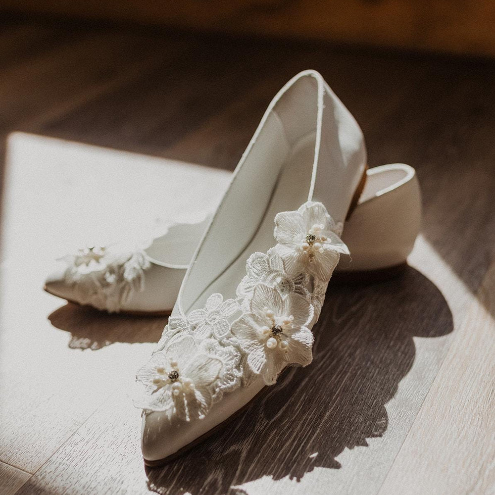 White wedding shoes with lace and pearl details on a wooden surface