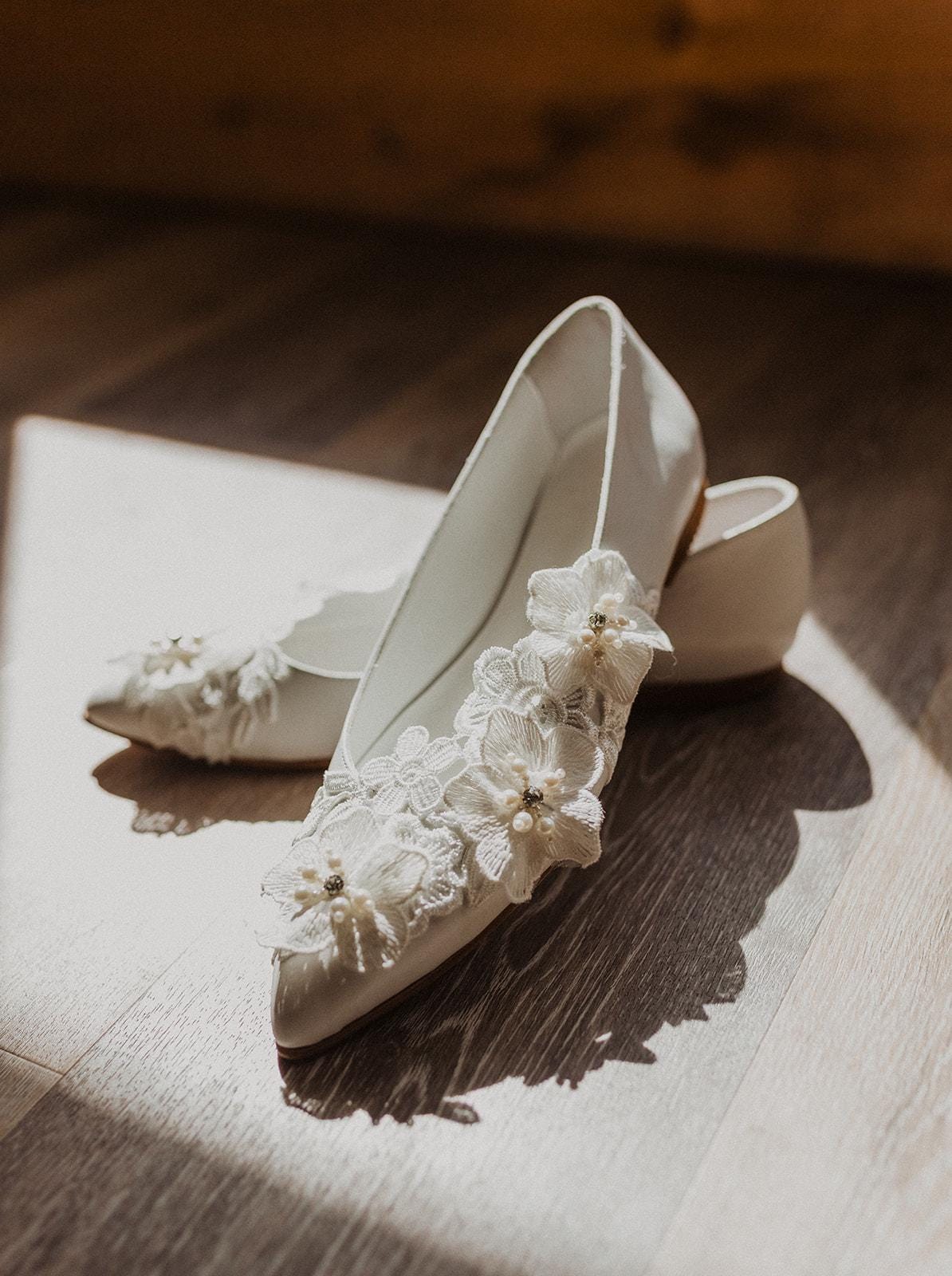 White wedding shoes with lace and pearl details on a wooden surface