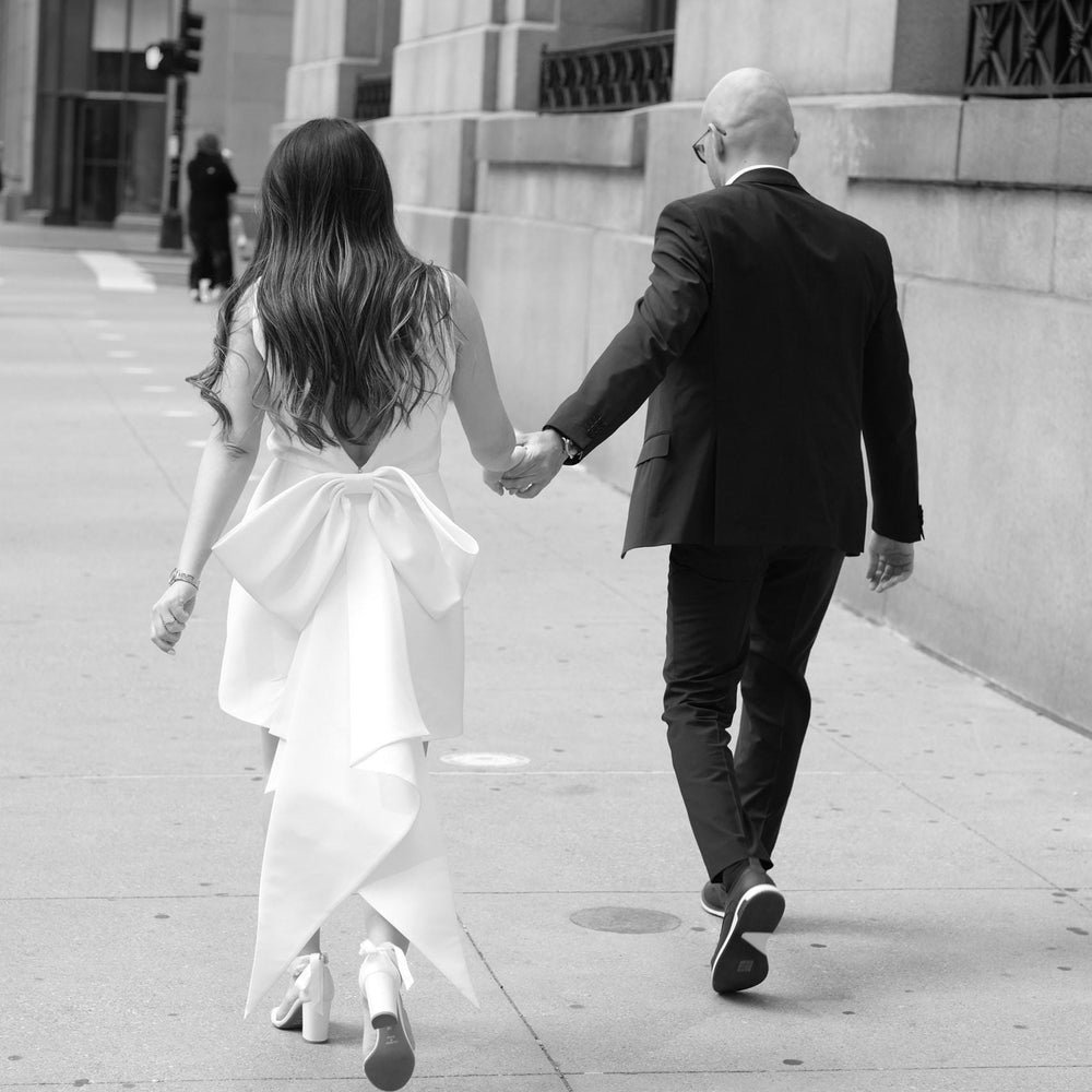 Man and woman holding hands and walking away from the camera on a city street.