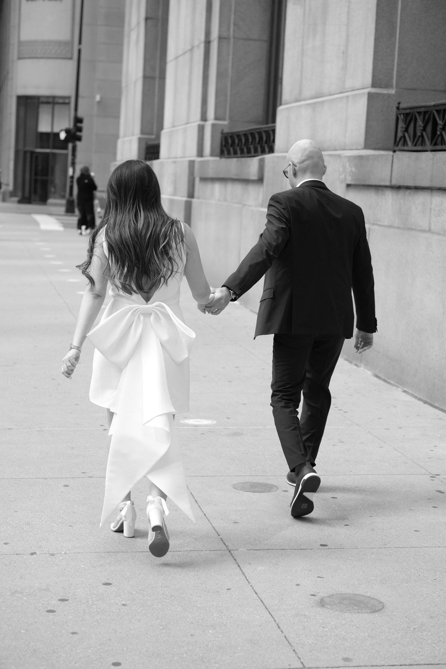 Man and woman holding hands and walking away from the camera on a city street.