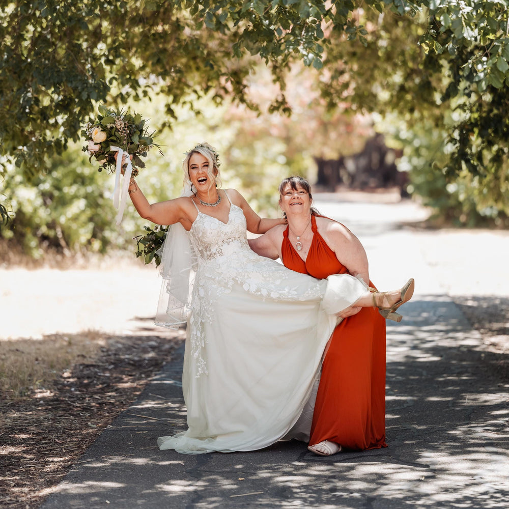 Two women in wedding dresses standing under a tree