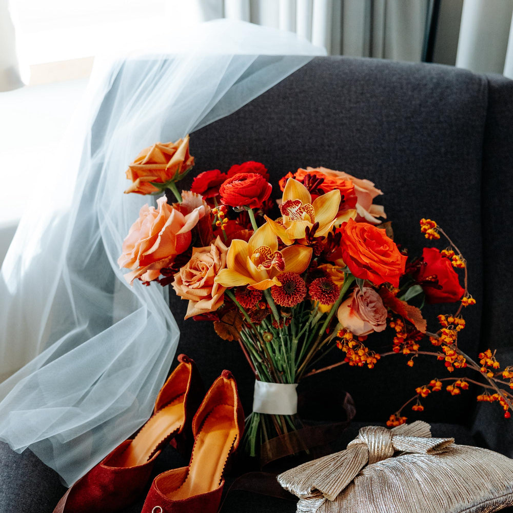 Bouquet of flowers, red shoes, and rings on a dark surface with light curtains in the background