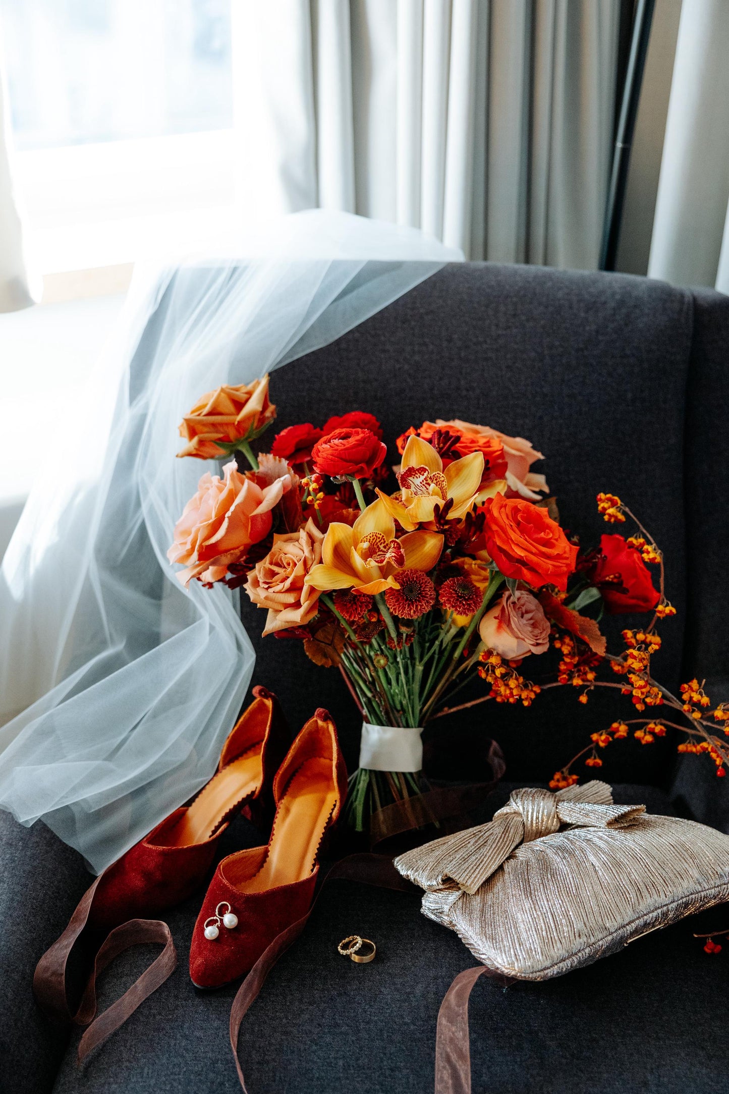 Bouquet of flowers, red shoes, and rings on a dark surface with light curtains in the background
